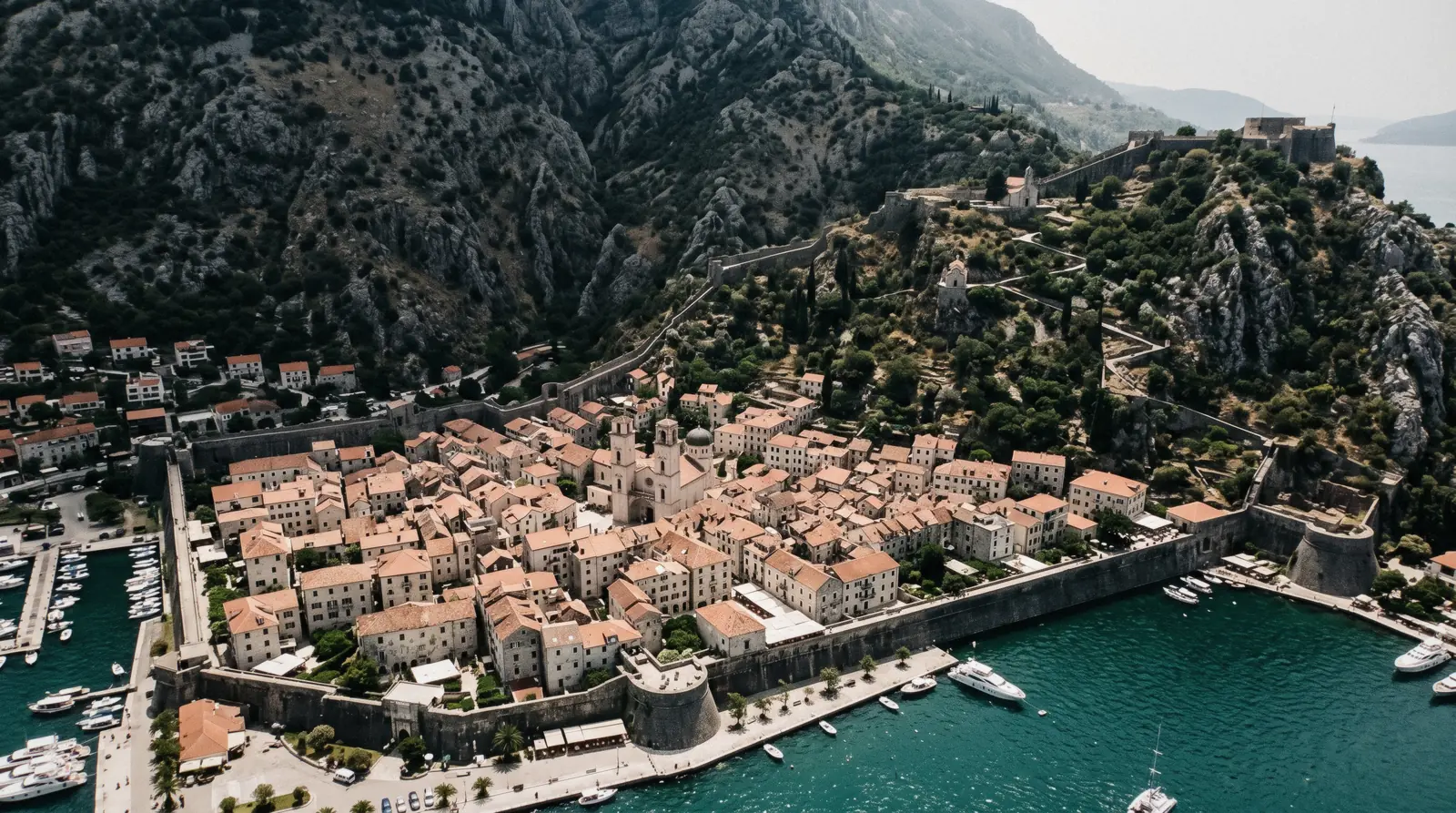 The walled town of Kotor seen from above with its pale stone roofs, the fortress mountain and the teal bay